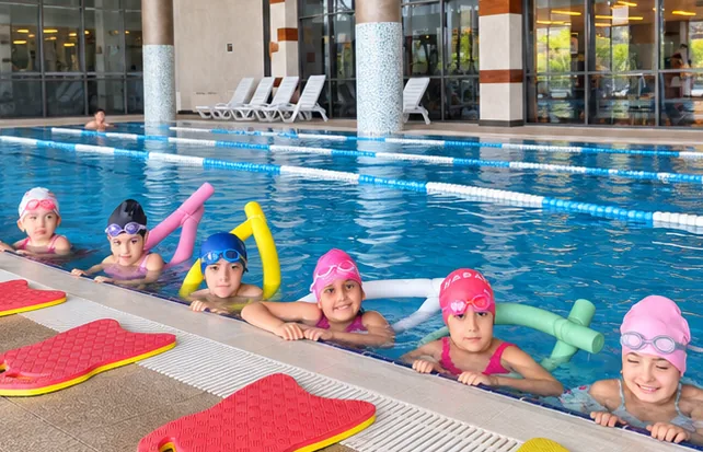 Havuz kenarında yüzme makarnalarıyla bekleyen çocuklar